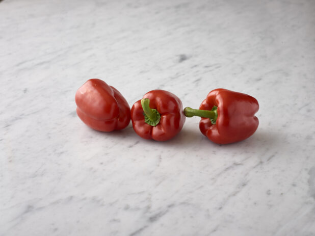 Whole fresh red bell peppers on a white marble background