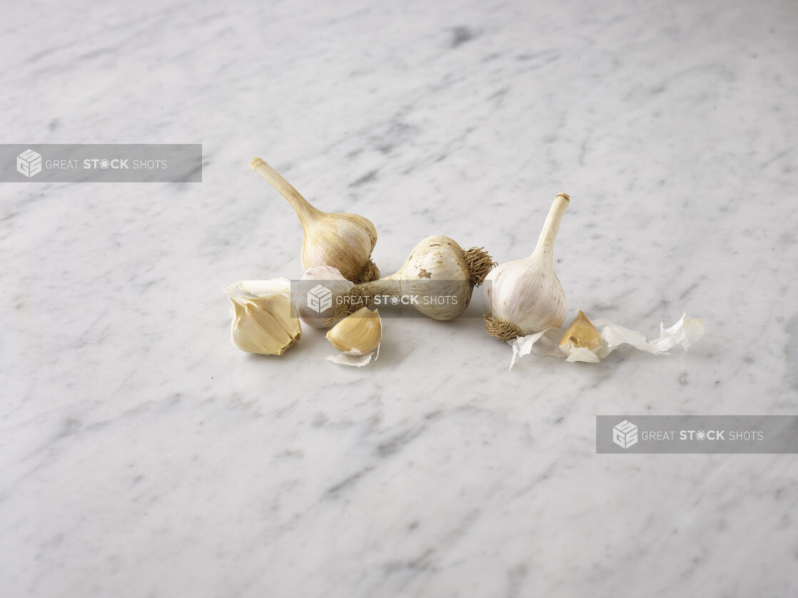 Whole garlic bulbs and cloves on a white marble background