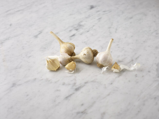Whole garlic bulbs and cloves on a white marble background