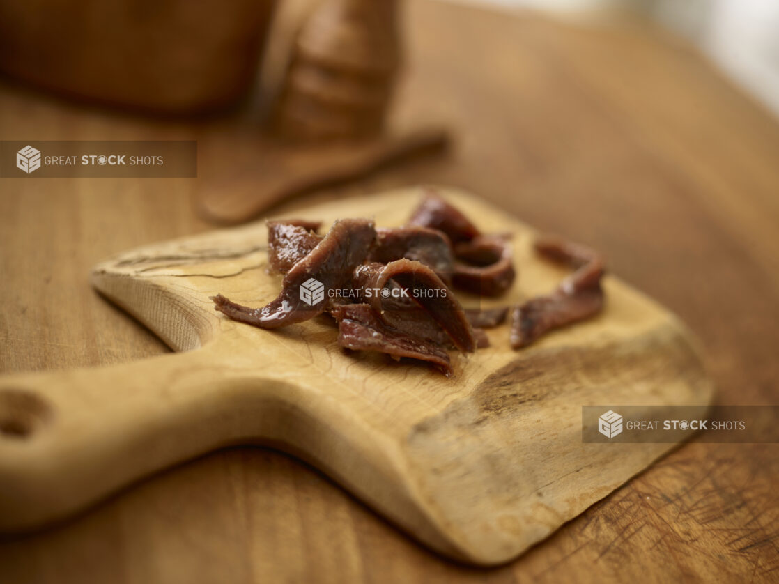 Anchovy fillets on a rustic wooden cutting board with a rustic wooden background with wooden accessories