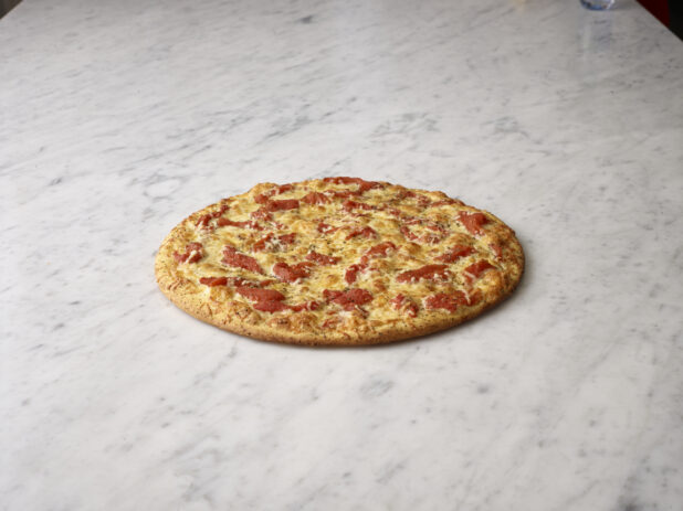 Whole roasted red pepper pizza on a white marble background