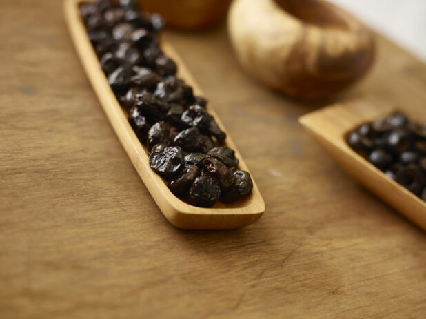 Whole pitted dates in a wooden rectangular platter on a rustic wooden background