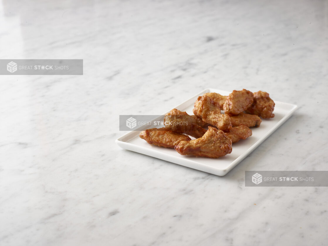 Buffalo chicken wings on a rectangular white platter on a white marble background