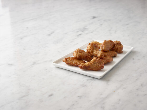 Buffalo chicken wings on a rectangular white platter on a white marble background