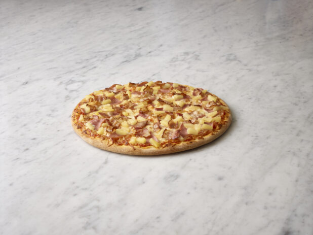 Whole Hawaiian pizza on a white marble background