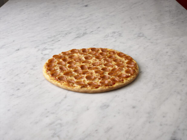 Whole pepperoni pizza on a white marble background