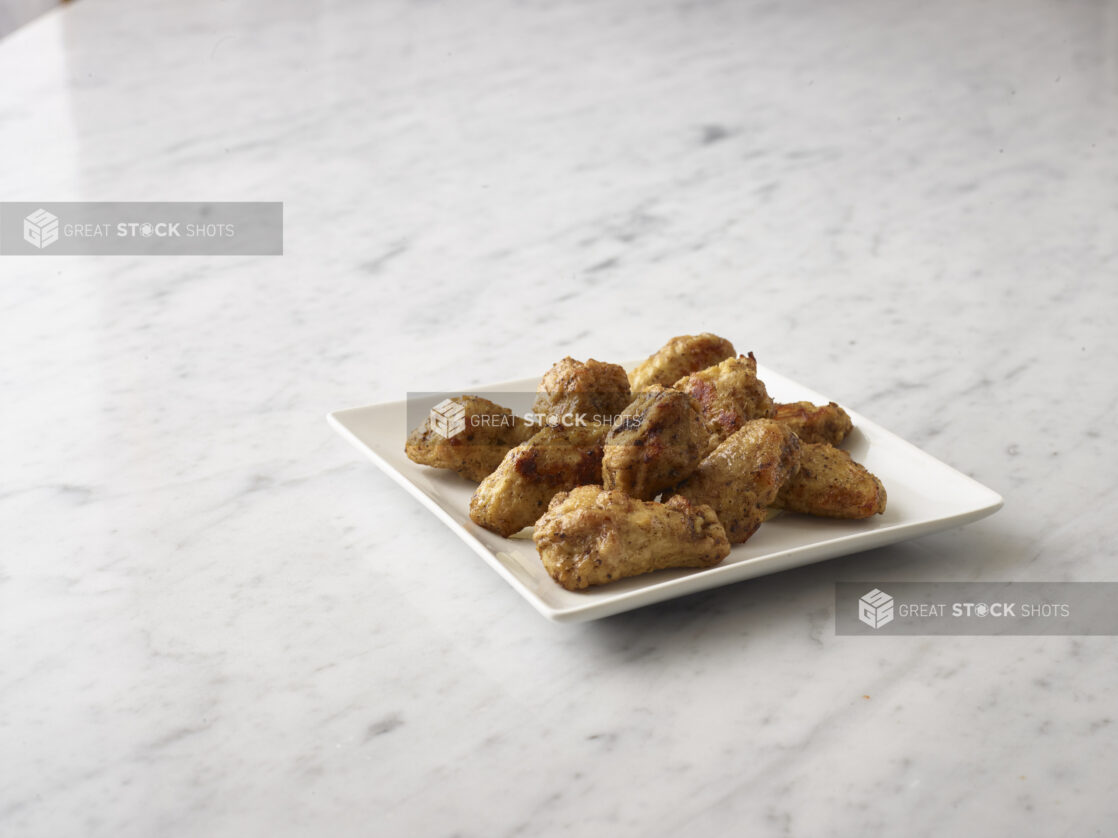 Breaded chicken wings on a white side plate on a white marble background