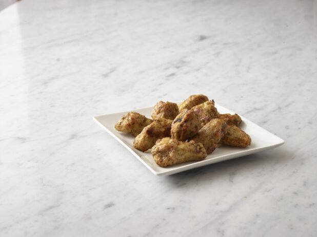 Breaded chicken wings on a white side plate on a white marble background