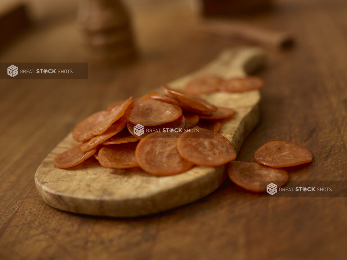 Slices of pepperoni on a wooden cutting board on a rustic wooden background