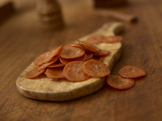 Slices of pepperoni on a wooden cutting board on a rustic wooden background