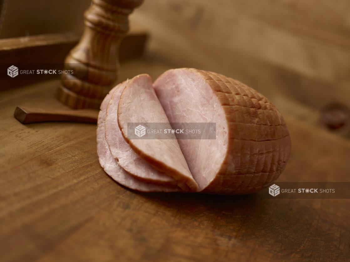 Whole boneless ham with a few slices on the ham on a rustic wooden background