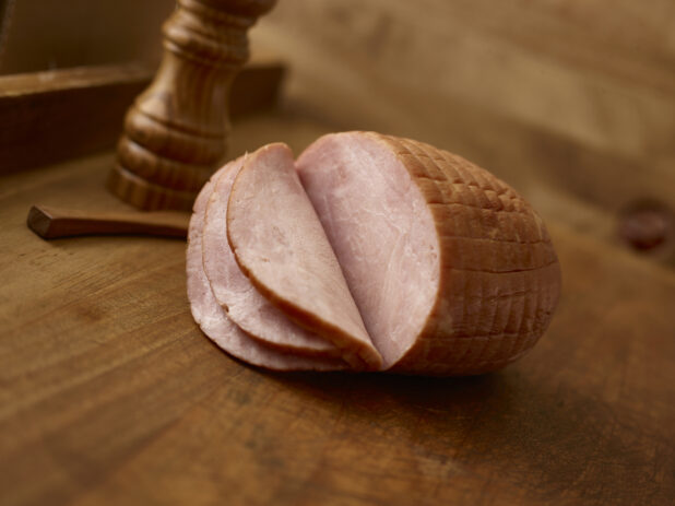 Whole boneless ham with a few slices on the ham on a rustic wooden background