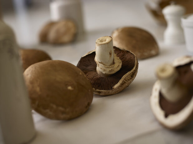 Whole portobello mushrooms in the foreground and background on a white linen background