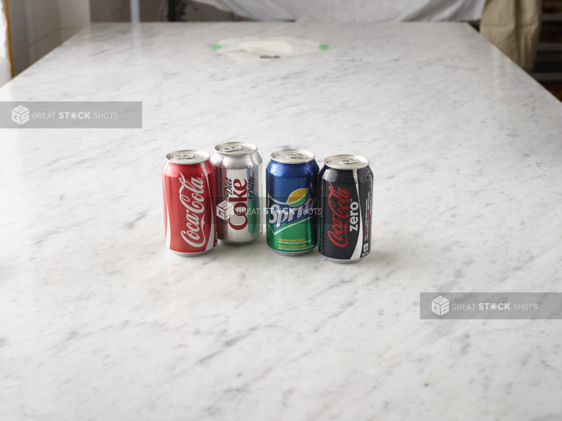 1 can of Coke, 1 can of Diet Coke, 1 can of Sprite and 1 Can of Coke Zero all on a white marble background