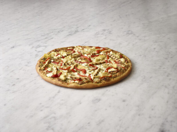 Whole pizza with chicken, artichokes, roasted red peppers and feta cheese on a white marble background