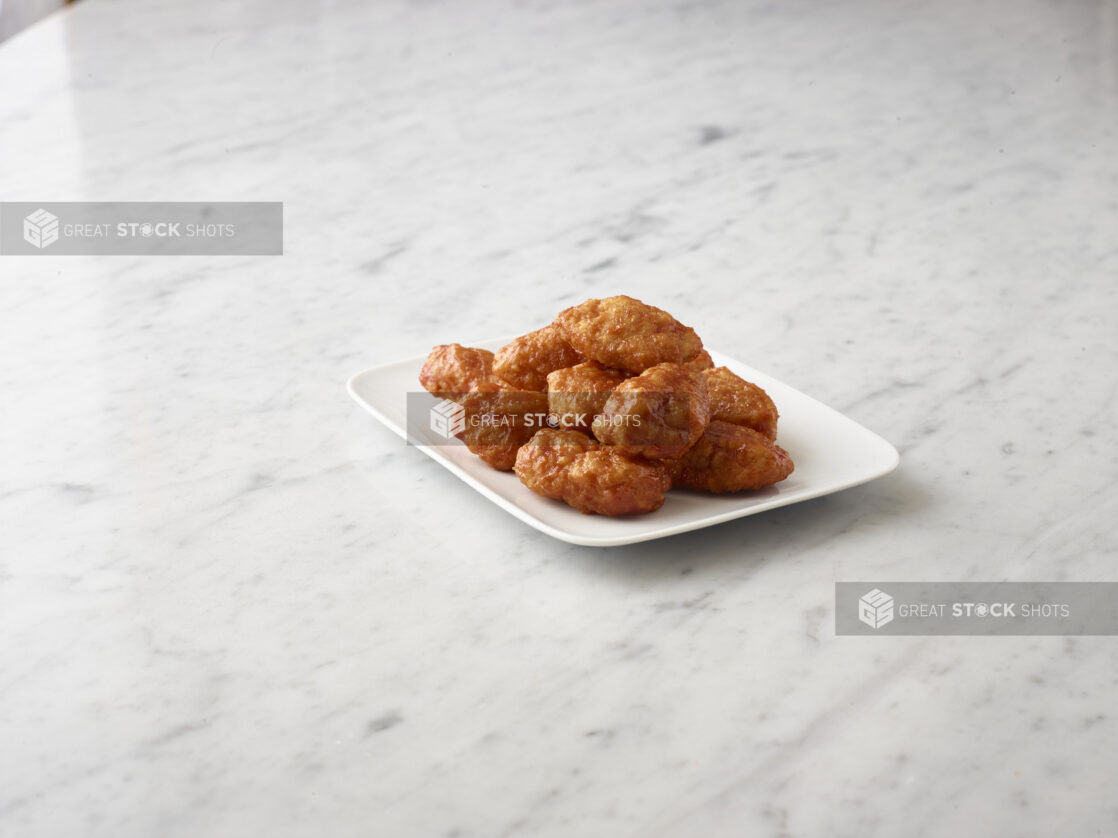 Buffalo style chicken wings on a square white side plate on a white marble background