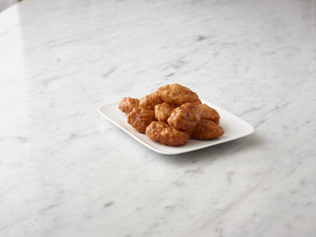 Buffalo style chicken wings on a square white side plate on a white marble background