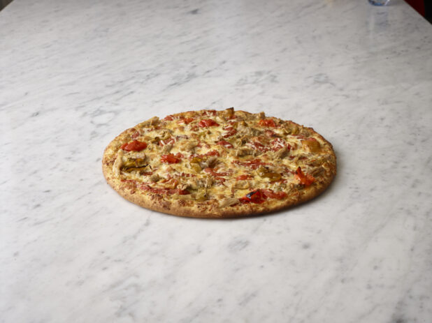 Whole 2 topping pizza with chicken and red peppers on a white marble background