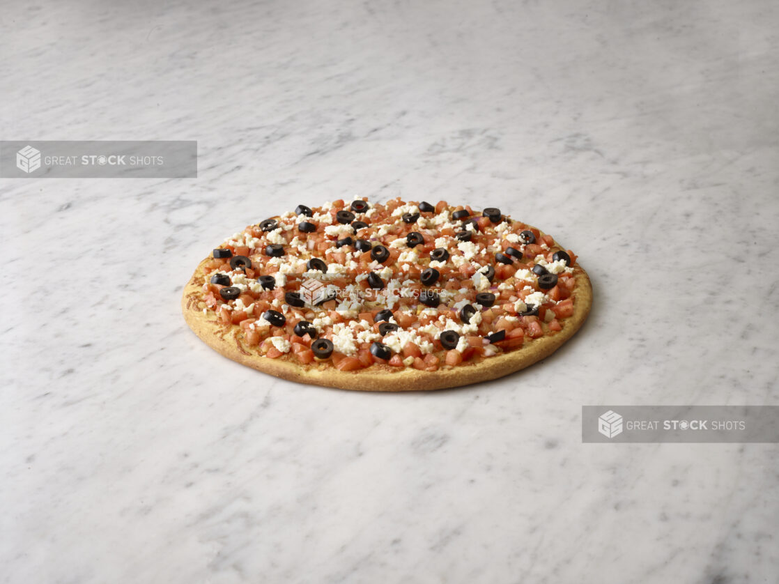 Whole pizza with bruschetta, black olives and feta on a white marble background