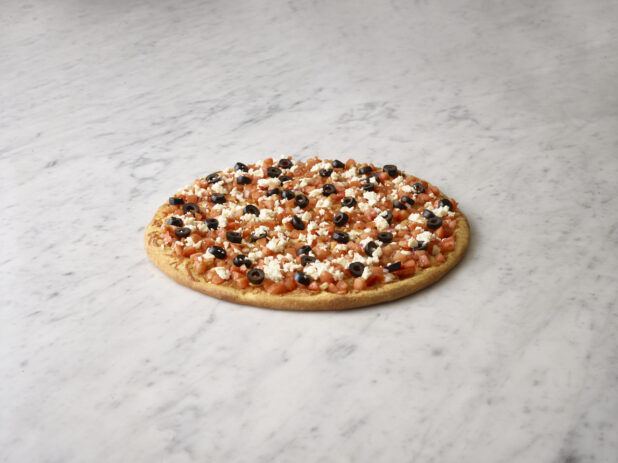 Whole pizza with bruschetta, black olives and feta on a white marble background