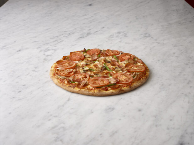 Whole 6 topping pizza with pepperoni, bacon, onions, tomatoes, green bell pepper, mushrooms on a white marble background