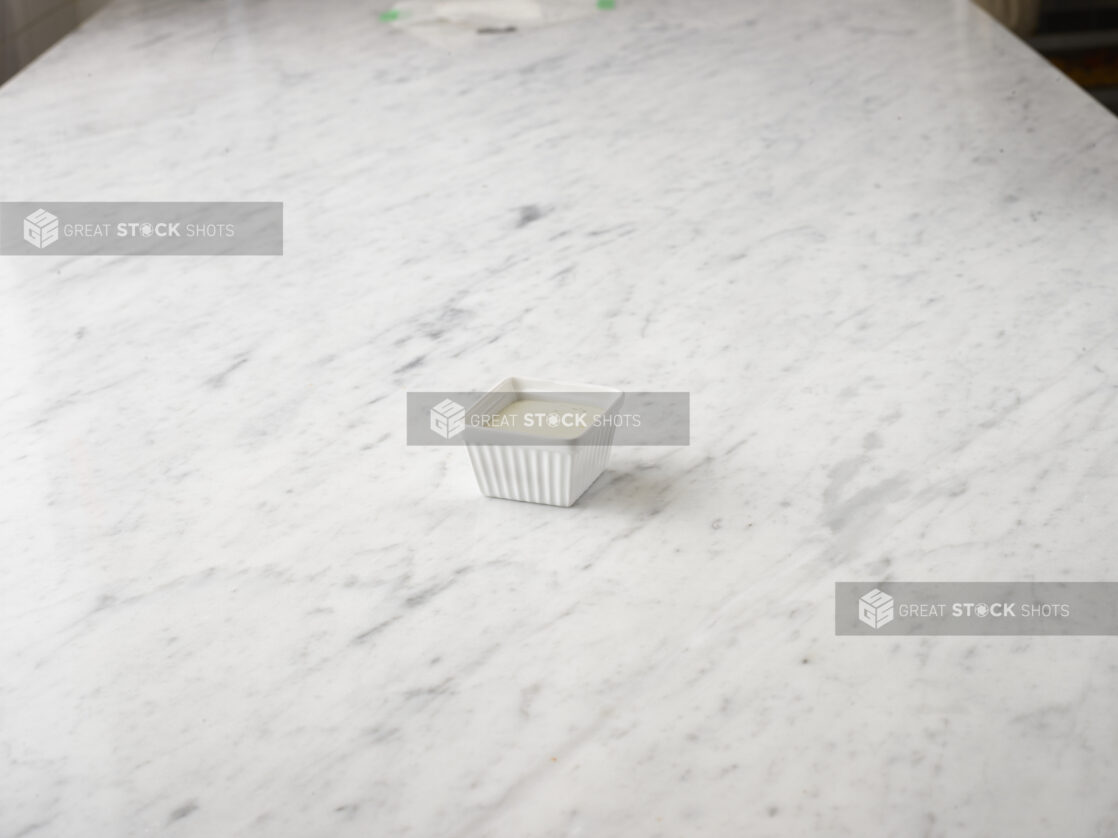 Grated parmesan cheese in a white square ramekin centered on a white marble background