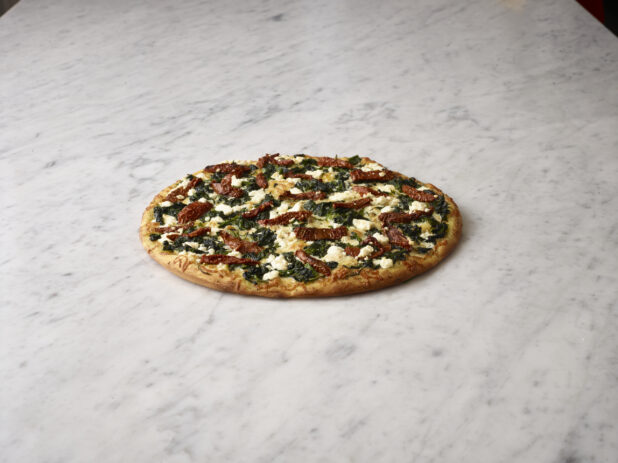 Whole 3 topping vegetarian pizza with spinach, sundried tomatoes and feta cheese on a white marble background