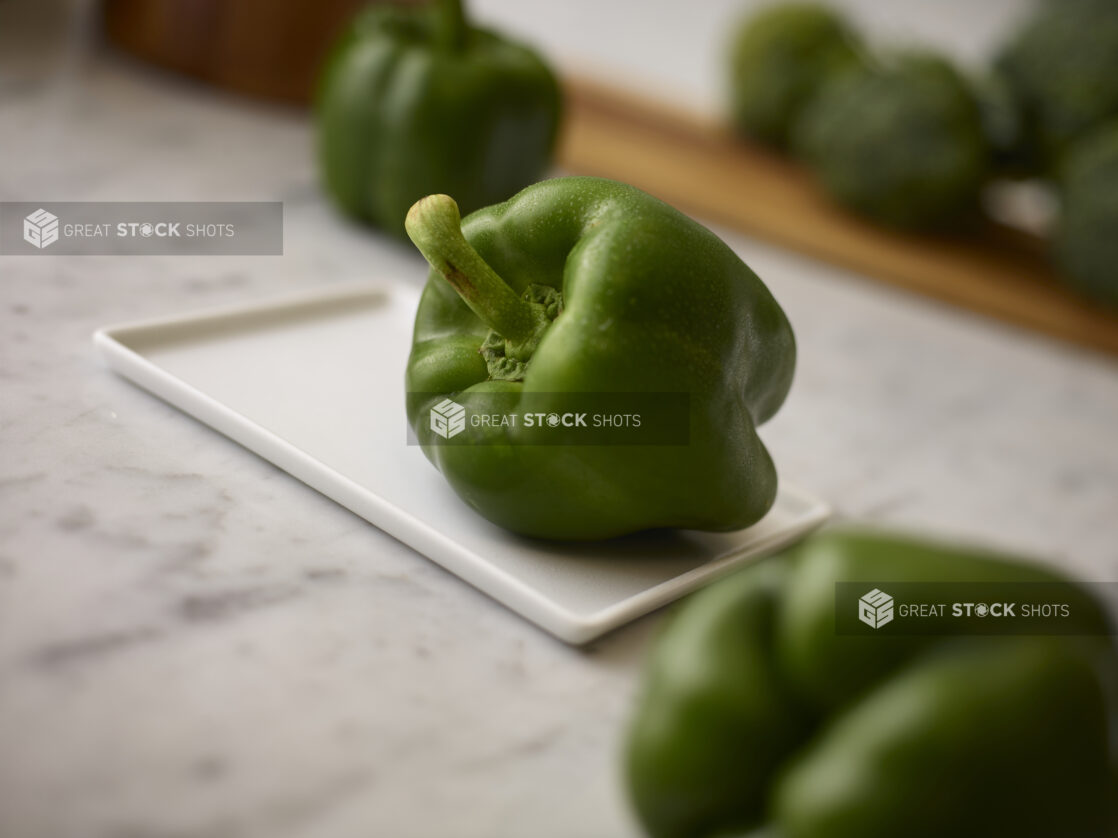 Whole fresh green bell peppers foreground, background and center view on a white marble background