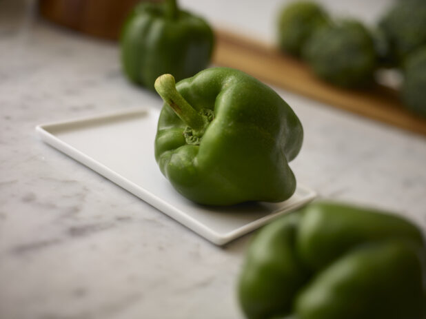 Whole fresh green bell peppers foreground, background and center view on a white marble background