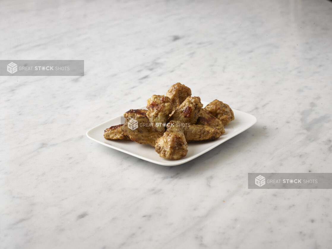 Fried chicken wings on a white side dish centered on a white marble background