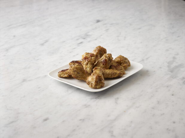 Fried chicken wings on a white side dish centered on a white marble background