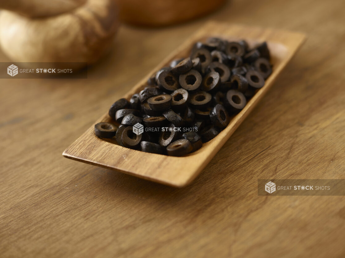 Black sliced olives in a wooden dish on a wooden background