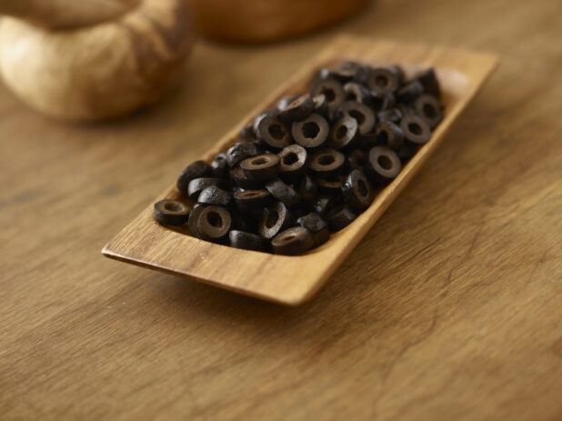 Black sliced olives in a wooden dish on a wooden background