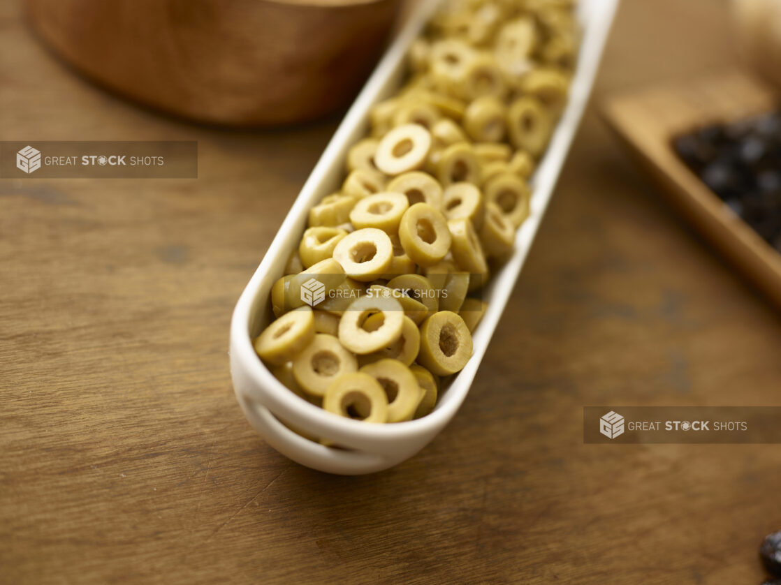 Sliced green olives in a long white oval side dish on a wooden background