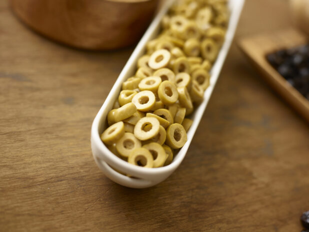 Sliced green olives in a long white oval side dish on a wooden background