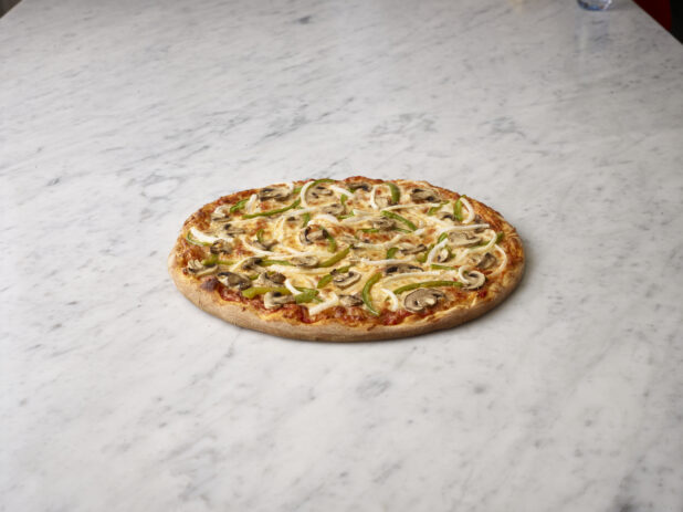 Vegetarian pizza, thin crust with mushrooms, green bell peppers and onions on a white marble background
