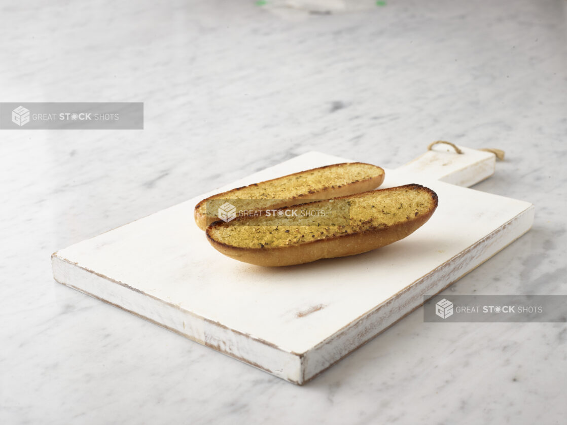 Garlic bread on a white wooden cutting board on a 45 degree angle on a white marble background