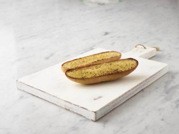 Garlic bread on a white wooden cutting board on a 45 degree angle on a white marble background