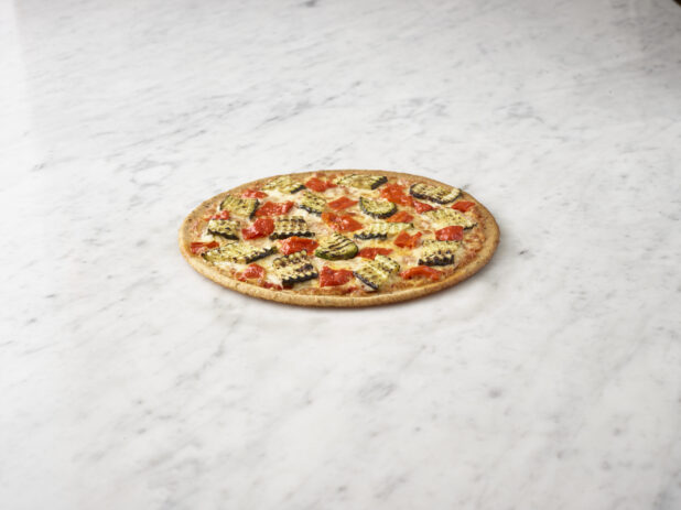 Gluten free thin crust vegetarian pizza with roasted bell peppers and zucchini on a white marble background on a 45 degree angle