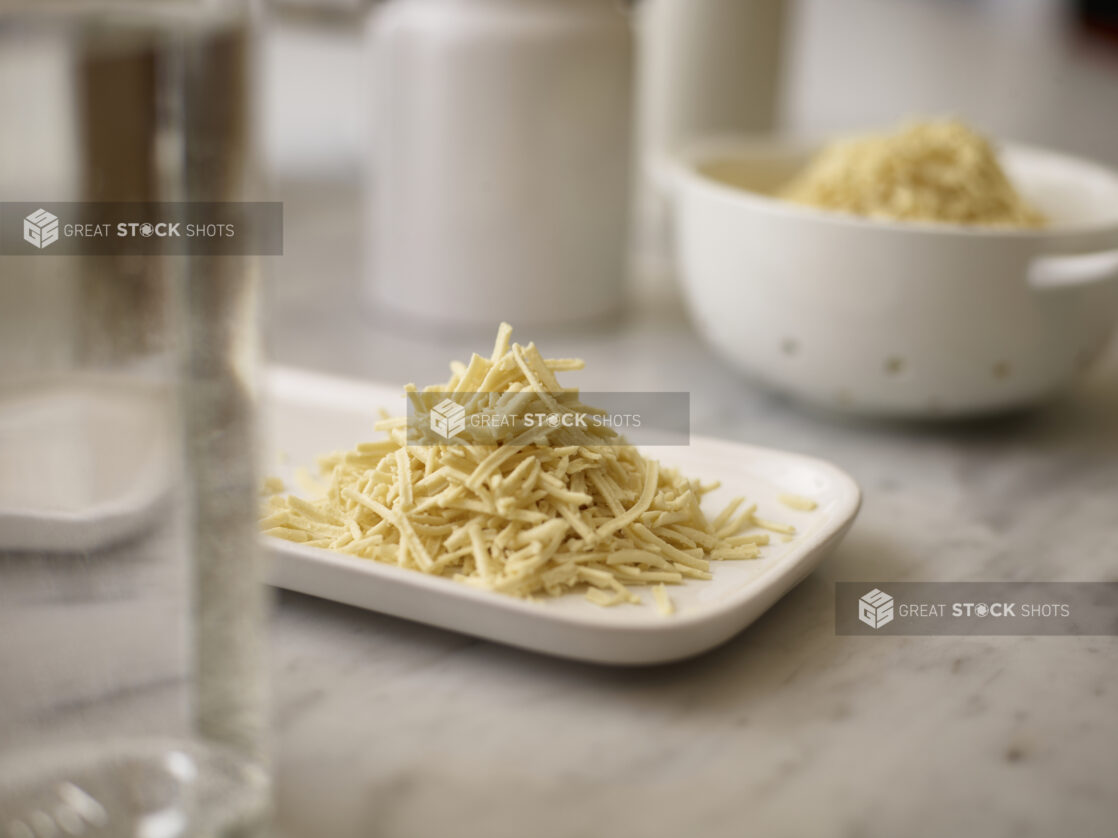 Shredded mozzarella on a white side plate on a marble table top with white accessories in the background