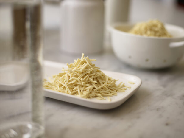 Shredded mozzarella on a white side plate on a marble table top with white accessories in the background
