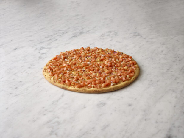 Whole bruschetta pizza on a white marble background