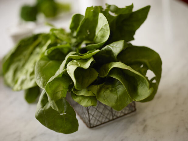 Close up view of whole fresh spinach in a decorative wire basket