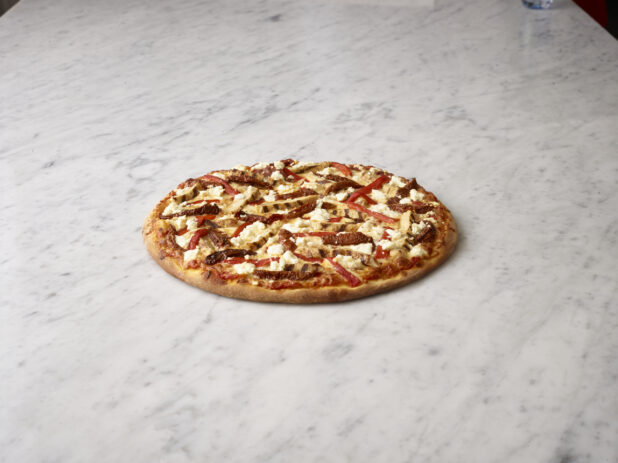 Whole pizza with chicken, sundried tomatoes, roasted red peppers and feta on a white marble background