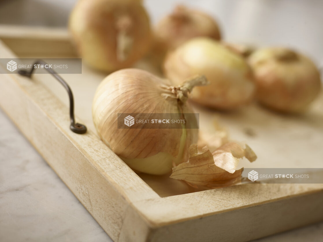 Close up view of whole onions with skin on, on a wooden tray, one in the foreground and 4 in the background