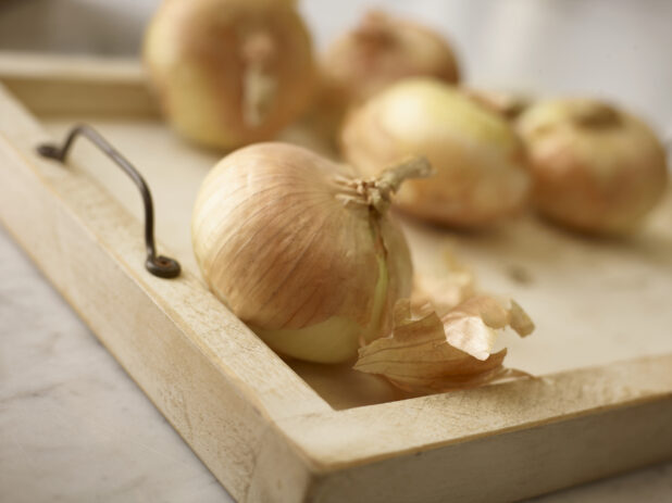 Close up view of whole onions with skin on, on a wooden tray, one in the foreground and 4 in the background