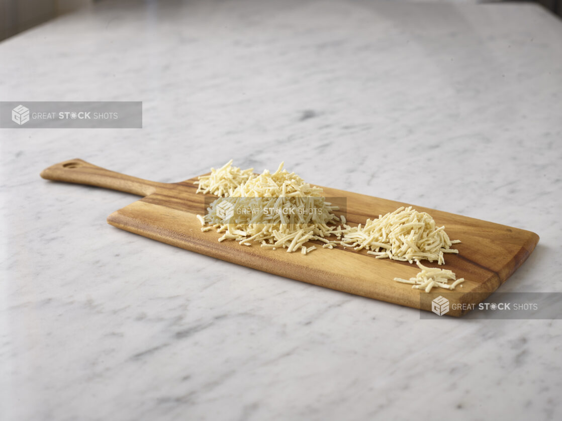 Shredded cheese on a wooden board on a white marble background