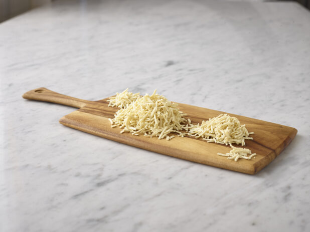 Shredded cheese on a wooden board on a white marble background