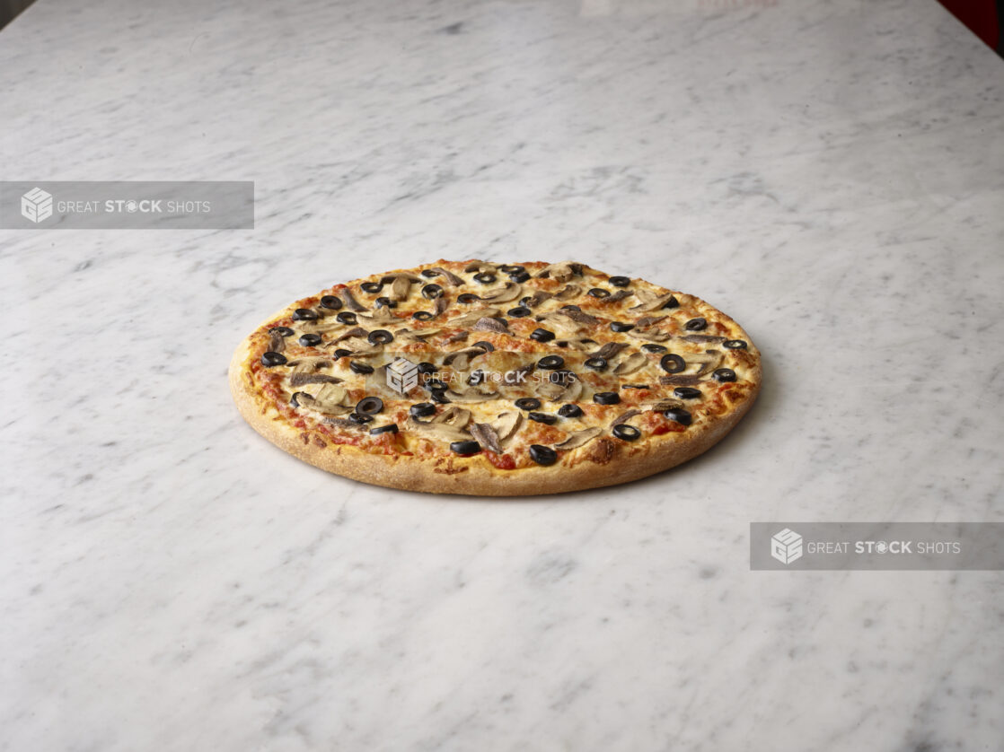 Whole mushroom and olive pizza on a white marble background