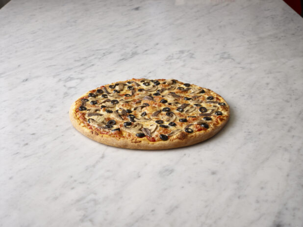 Whole mushroom and olive pizza on a white marble background